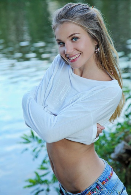 Adorable teen Lola Krit proudly shows her bald pussy by a pond 84375765