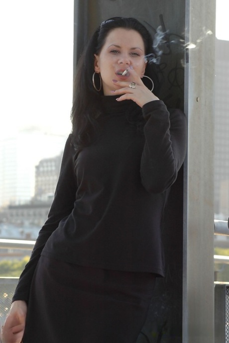 Fully clothed brunette lights up a cigarette with her sunglasses atop her head 80845498