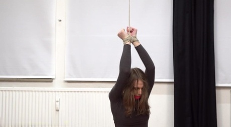 Barefoot girl dons a ball gag before being tied at her wrists on her knees 73875176